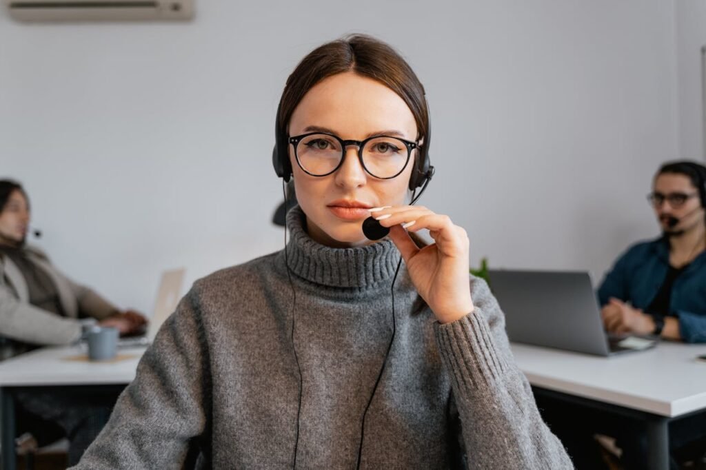 A focused call center agent with glasses and headset in a modern office setting.